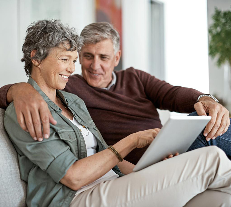 mature couple using a digital tablet while relaxing on their sofa